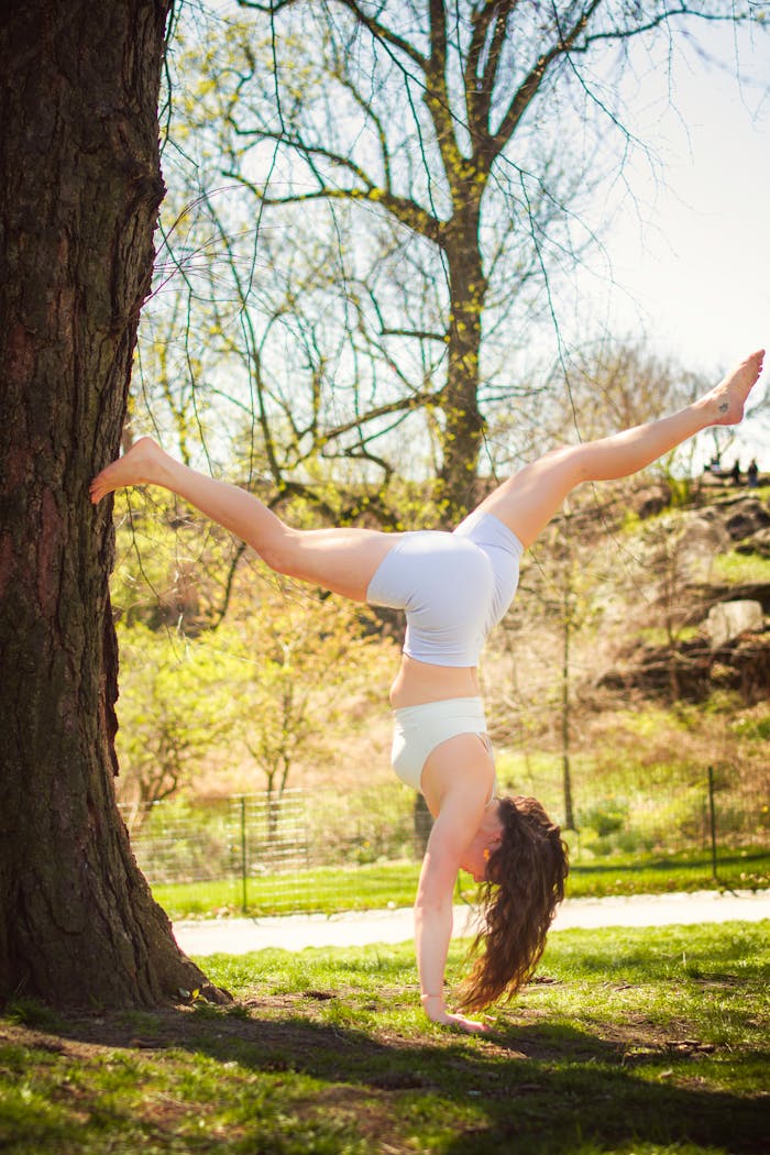 A woman performs a handstand against a tree in Central Park, embracing outdoor fitness.