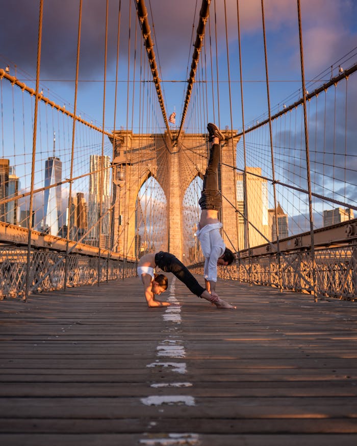 Couple practicing acro yoga exercises on the iconic Brooklyn Bridge during a beautiful sunrise in New York City.