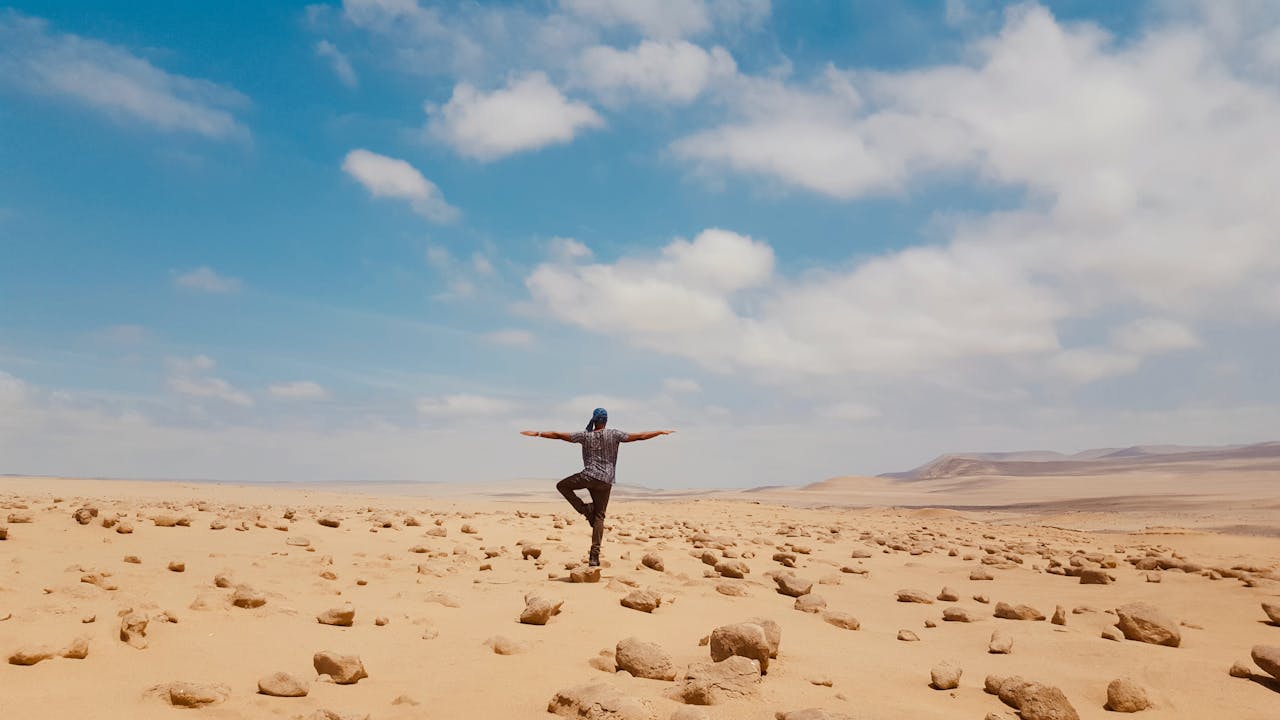 A man balancing in a serene yoga pose amidst the vast desert landscape of Huacachina, Peru.