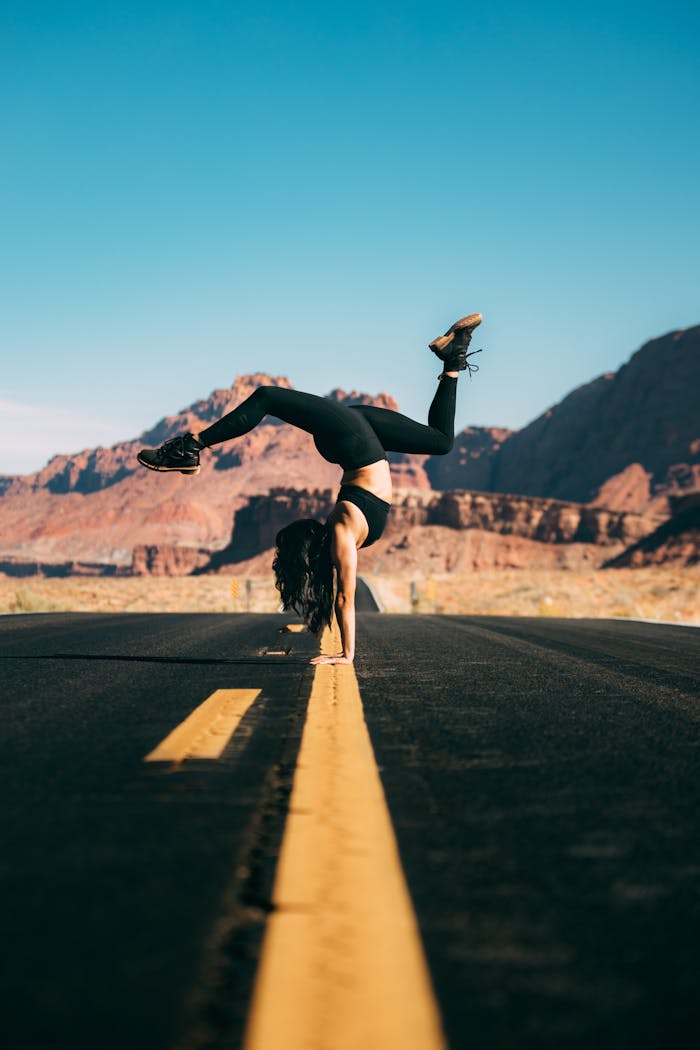 Woman in sportswear doing a handstand on a desert road against a blue sky.